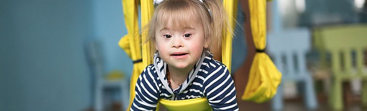 Lachendes Kind mit Down Syndrom auf Schaukel; anderes Kind schubst an